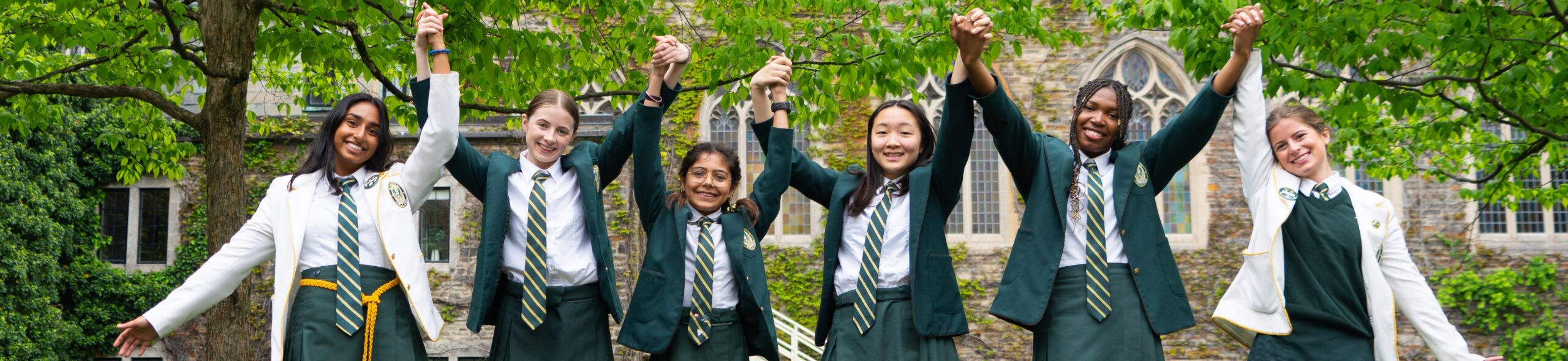 Upper School students link hands in the North Quad, smiling and holding their hands in the air.